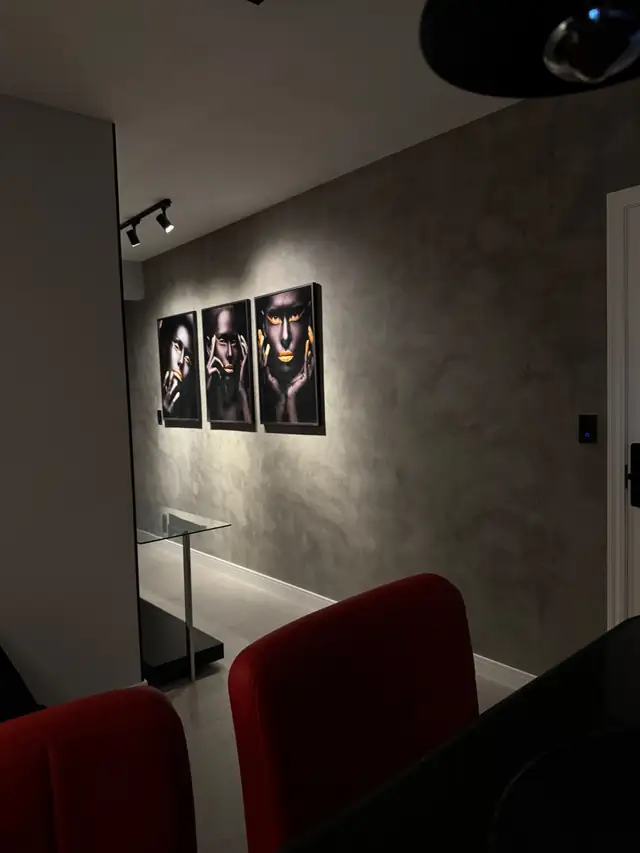 Ambiente interno com parede em efeito cimento queimado e quadros iluminados por spots