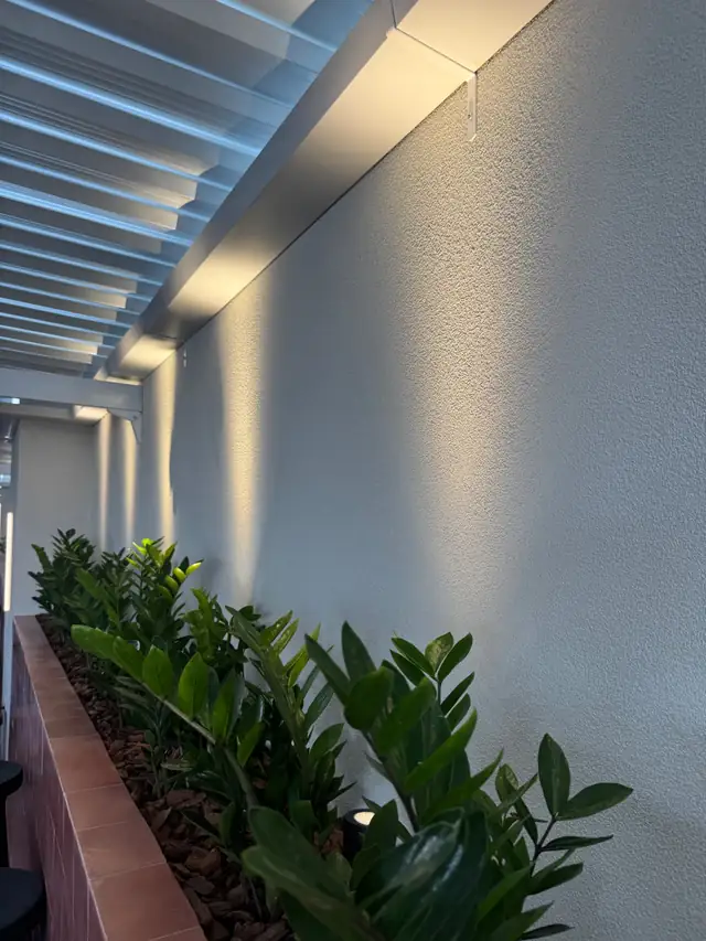 Corredor externo com parede em textura Cristaline, floreira e iluminação rasante